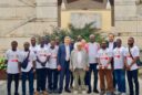 A mixed group of young Ghanaian men and middle-aged Italian businessmen pose for a group portrait in front of a large limestone building.